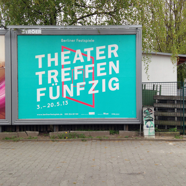 Minimalist sky-blue billboard on a city street reading "Theater Treffen Fünfzig"