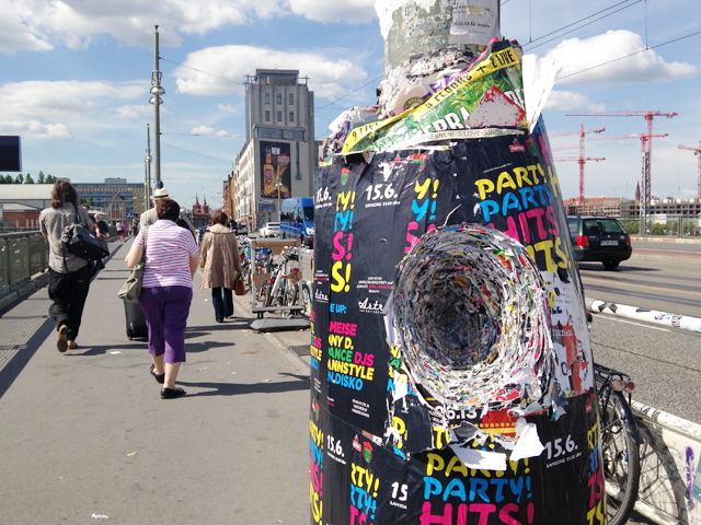 Thick hoarding of posters on a busy street, with a deep hole cut in the posters