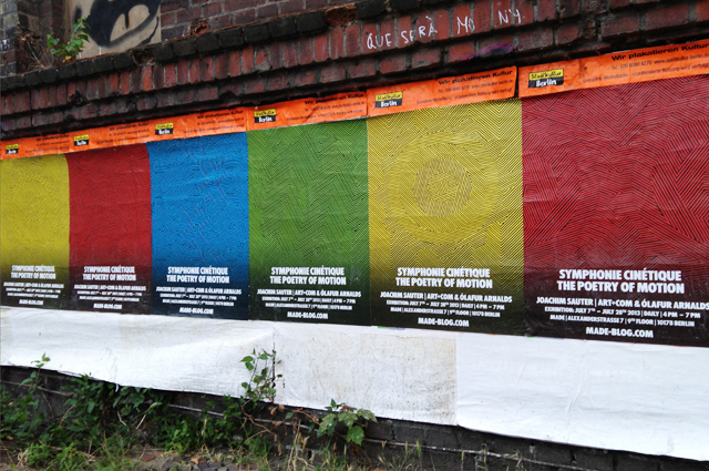 Row of four posters on a brick wall, in bright solid colors with geometric line graphics.