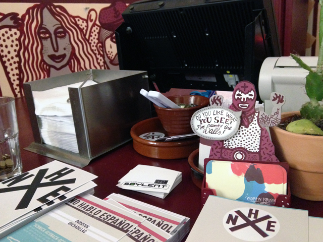 Cluttered shop counter with person-shaped business card holder reading "Do you like what you see? I painted the walls!"