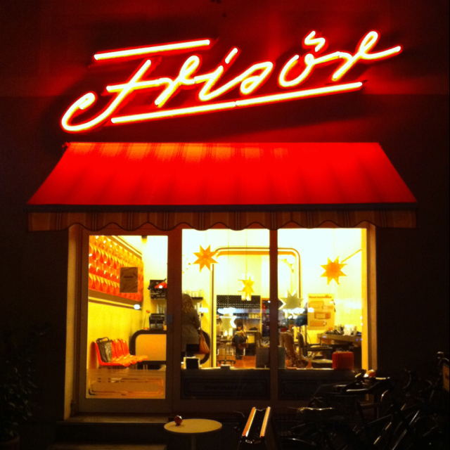 Neon lettering "Frisör" above a salon window at night