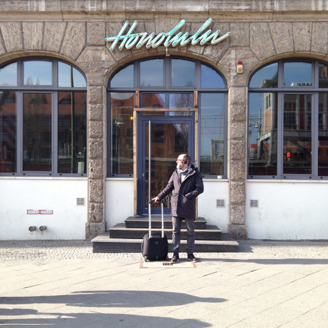 Neon sign reading "Honolulu" over doorway; man with suitcase standing in front of the door