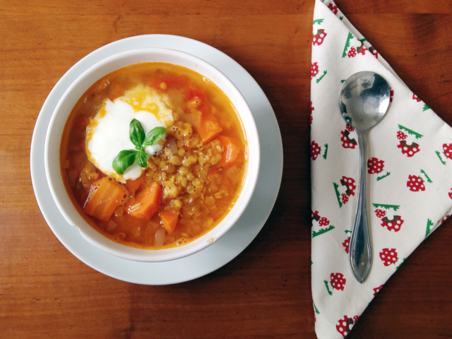 Bowl of orange soup with lentils, carrots, and yogurt; spoon on a cloth napkin.